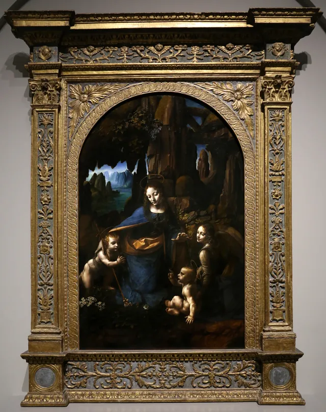Felsgrottenmadonna, Londoner Fassung: fotografiert in ihrem hohen, vergoldeten Altarrahmen mit Säulen. Darin kniet Maria in einer Grotte zwischen den beiden Kindern, rechts ein Engel. Eine Reproduktion.